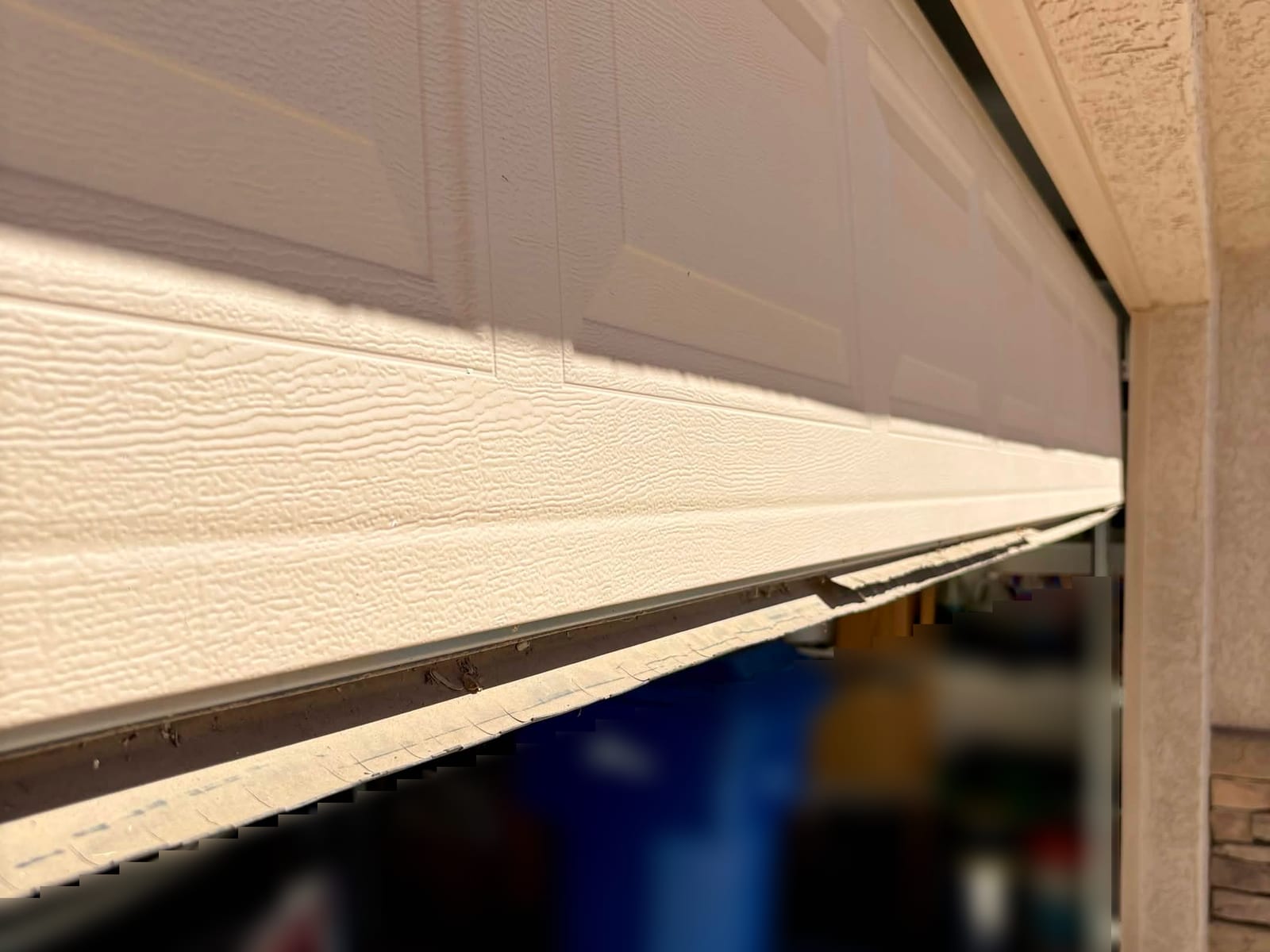 Before: cracked bottom seal pulling away from the lower edge of a garage door, seen from the driveway in Mesa